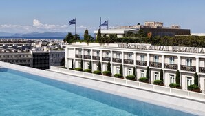 A hotel with a pool, flags, and a view of a historic building in the background. - Athens Capital Center Hotel-MGallery Collection (Athens)