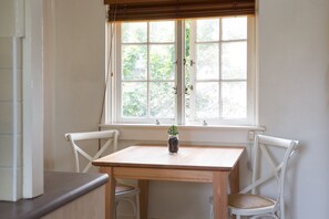 A room with a wooden table and two white chairs, a window with blinds, and a small potted plant on the table.