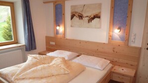 A wooden bed with white bedding, a nightstand, and a wall-mounted light fixture. - Holiday apartment valley view (Curon Venosta)