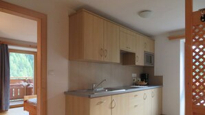A kitchen with wooden cabinets, a stainless steel sink, and a microwave. - Holiday apartment valley view (Curon Venosta)