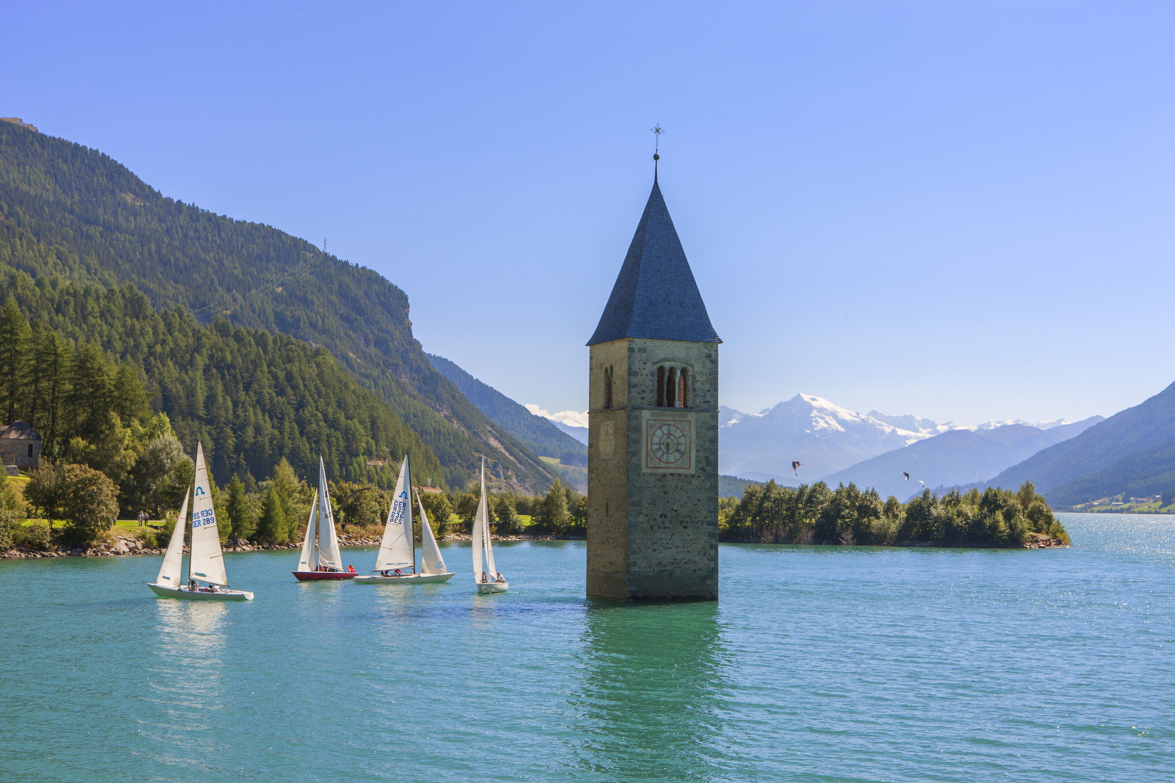 Ein Turm mit einer Uhr an einem See, umgeben von Segelbooten und Bergen.