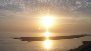 A beach scene with the sun low on the horizon, casting a warm glow over the water and sand. - ---- bungalow 5 ---- (Les Mathes)