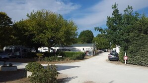 A rural road with a white building, parked vehicles, and a speed limit sign. - ---- bungalow 5 ---- (Les Mathes)