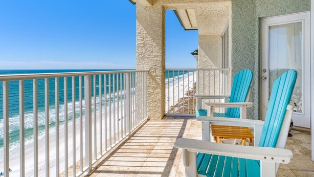 Een balkon met uitzicht op de oceaan, twee turquoise stoelen en een klein houten tafeltje.