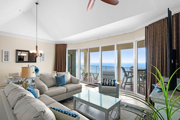 A spacious living room with a glass coffee table, beige sofas, a large mirror, and a view of the ocean through sliding glass doors.
