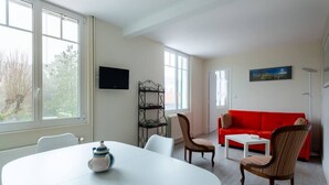 Una sala de estar moderna con una mesa blanca, un sofá rojo y un televisor montado en la pared.