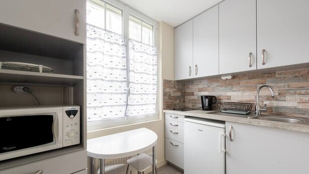 Una cocina compacta con armarios blancos, microondas, cafetera y lavamanos.