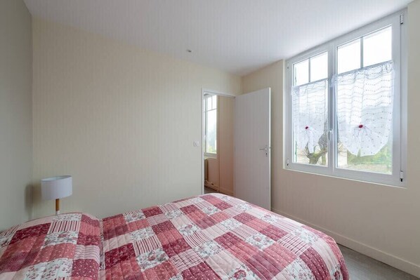 A bedroom with a bed, a window with curtains, and a door.