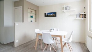 Un comedor con una mesa y sillas blancas, un cuadro en la pared y estantes con objetos.