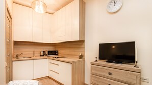 A compact kitchen with a microwave, sink, and wooden cabinets. A flat-screen TV is mounted on a wooden dresser.