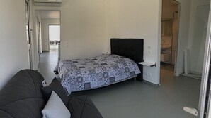 Moderni makuuhuone, jossa on sänky, yöpöytä, tummanvärinen sohva ja näkymä kylpyhuoneeseen avonaisen oven kautta.