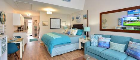 A well-lit bedroom with a bed, a sitting area with a sofa, a dining table, and a kitchen area.