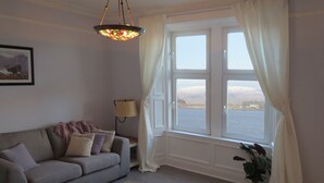 A cozy living room with a grey sofa, a patterned rug, a floor lamp, and a window with curtains. - 3 Oban - fantastic sea view apartment (Oban)