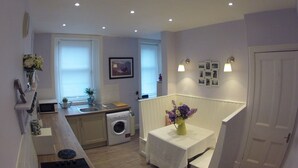 A compact kitchen with a washing machine, a sink, and a small table with a vase of flowers. - 3 Oban - fantastic sea view apartment (Oban)