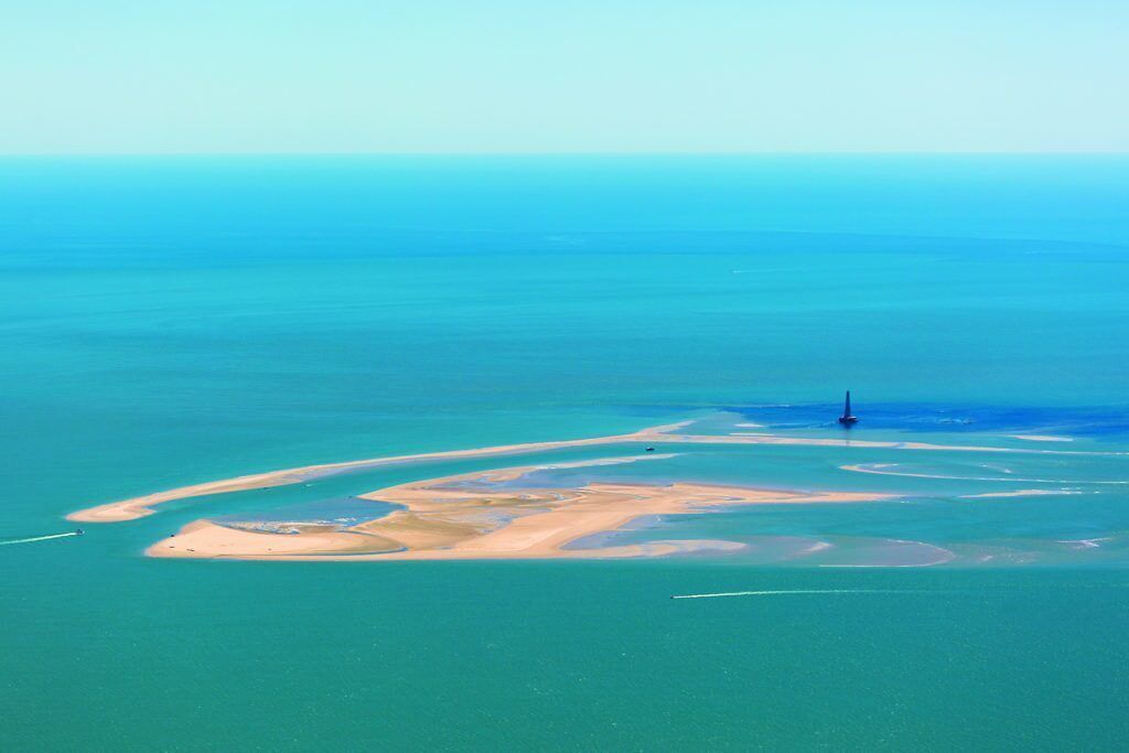 Vue aérienne d’une zone côtière avec un phare, des plages de sable et une eau d’un bleu limpide.