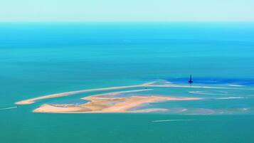 Vue aérienne d’une zone côtière avec un phare, des plages de sable et une eau d’un bleu limpide.