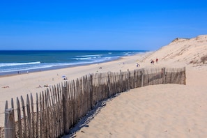 Ein sandiger Strand mit einer Holzlattenzaun, einem strahlend blauen Himmel und dem Meer im Hintergrund.