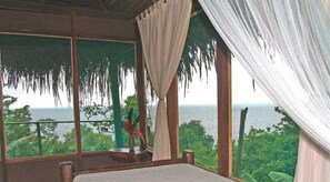 A room with a large window overlooking a lush landscape and the sea.