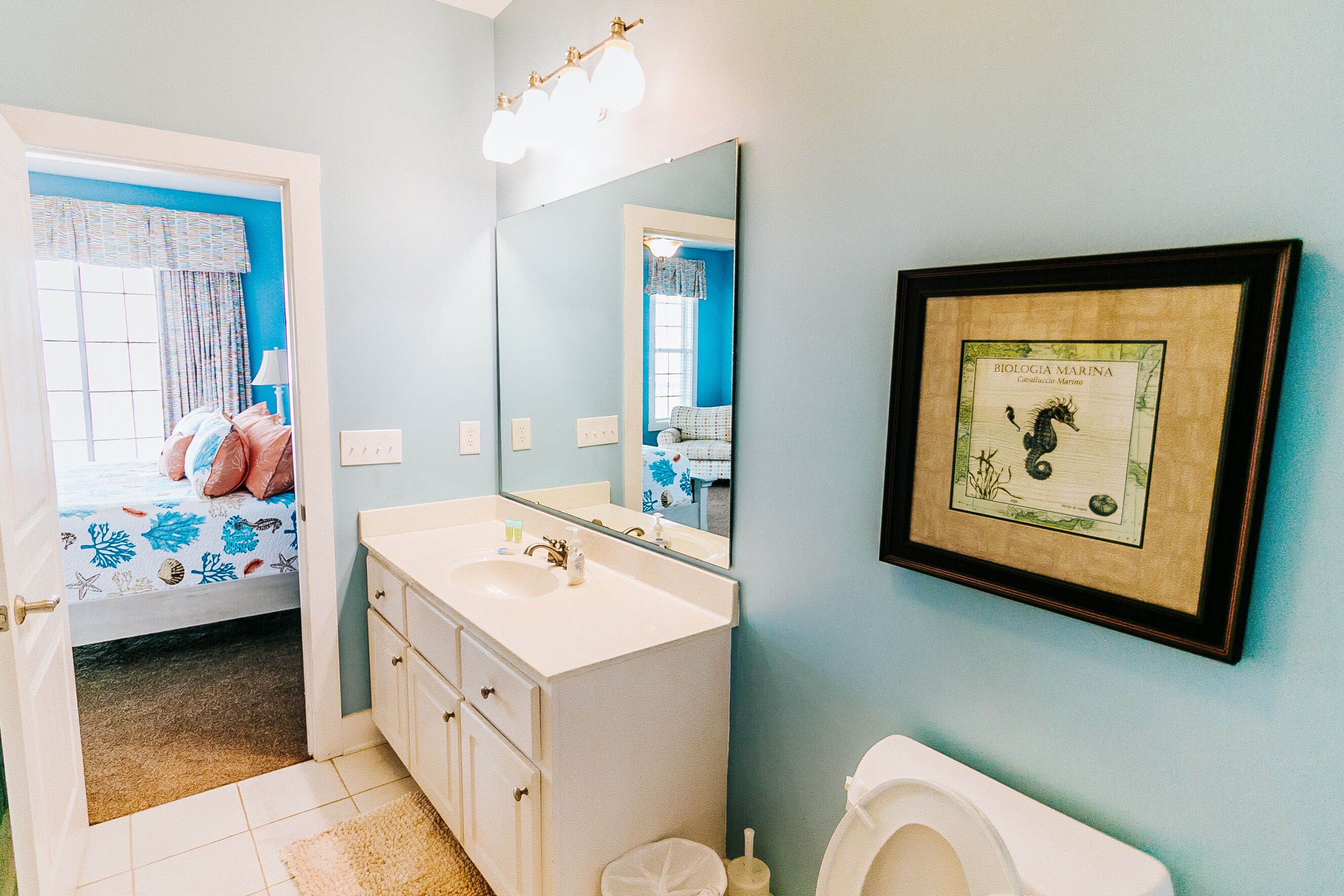 A bathroom with a white sink, mirror, and toilet. There is a framed marine biology picture on the wall.