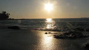 Una spiaggia con il sole che tramonta sull'acqua, creando un riflesso sulla sabbia.