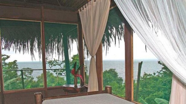Una habitación con un amplio ventanal que da a un paisaje exuberante y al mar.