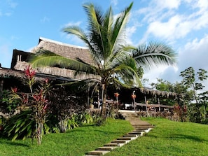 Un complexe hôtelier tropical doté d’un bâtiment à toit de chaume, d’un palmier et d’un escalier en pierre menant à l’entrée.