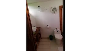 A compact bathroom with a toilet, sink, and mirror, plus a wooden cabinet and trash bin.