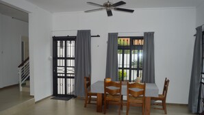 A dining area with a table and chairs, a ceiling fan, and a view through a window with curtains.