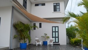 A covered outdoor area with a patterned floor, two white chairs, and potted plants.