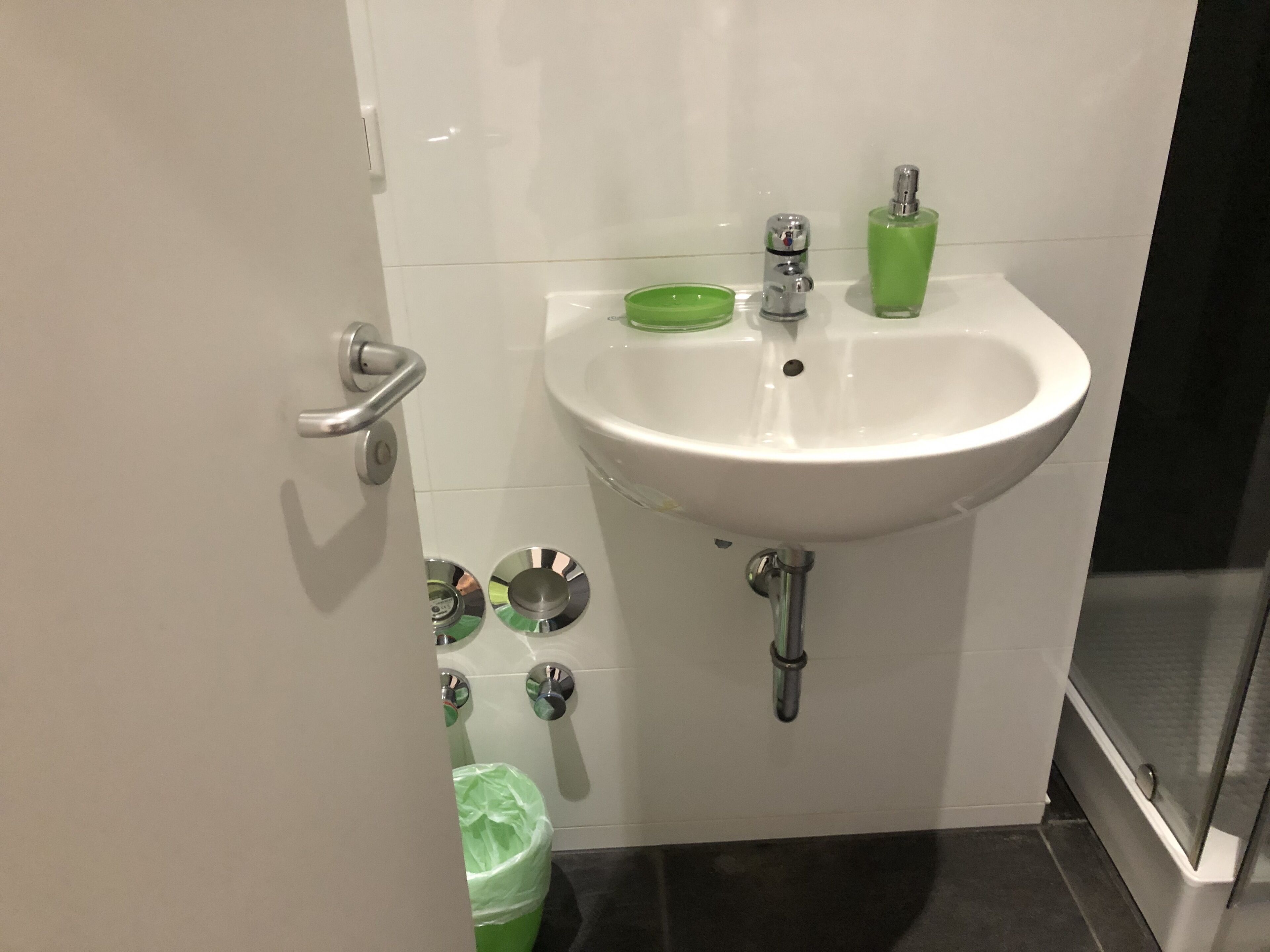 A bathroom with a white sink, green soap dish, and a green trash bin.