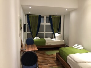 A small hotel room with two single beds, a wooden desk, a chair, and a window with curtains. - Pension Baku (Fuerth)
