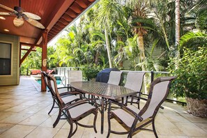 Eine Terrasse im Freien mit einem runden Tisch und Stühlen, umgeben von üppiger tropischer Vegetation.