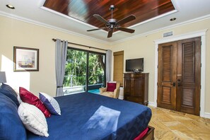 Ein Schlafzimmer mit einem Bett, Deckenventilator, Fernseher und einer Glasschiebetür, die auf einen Balkon führt.