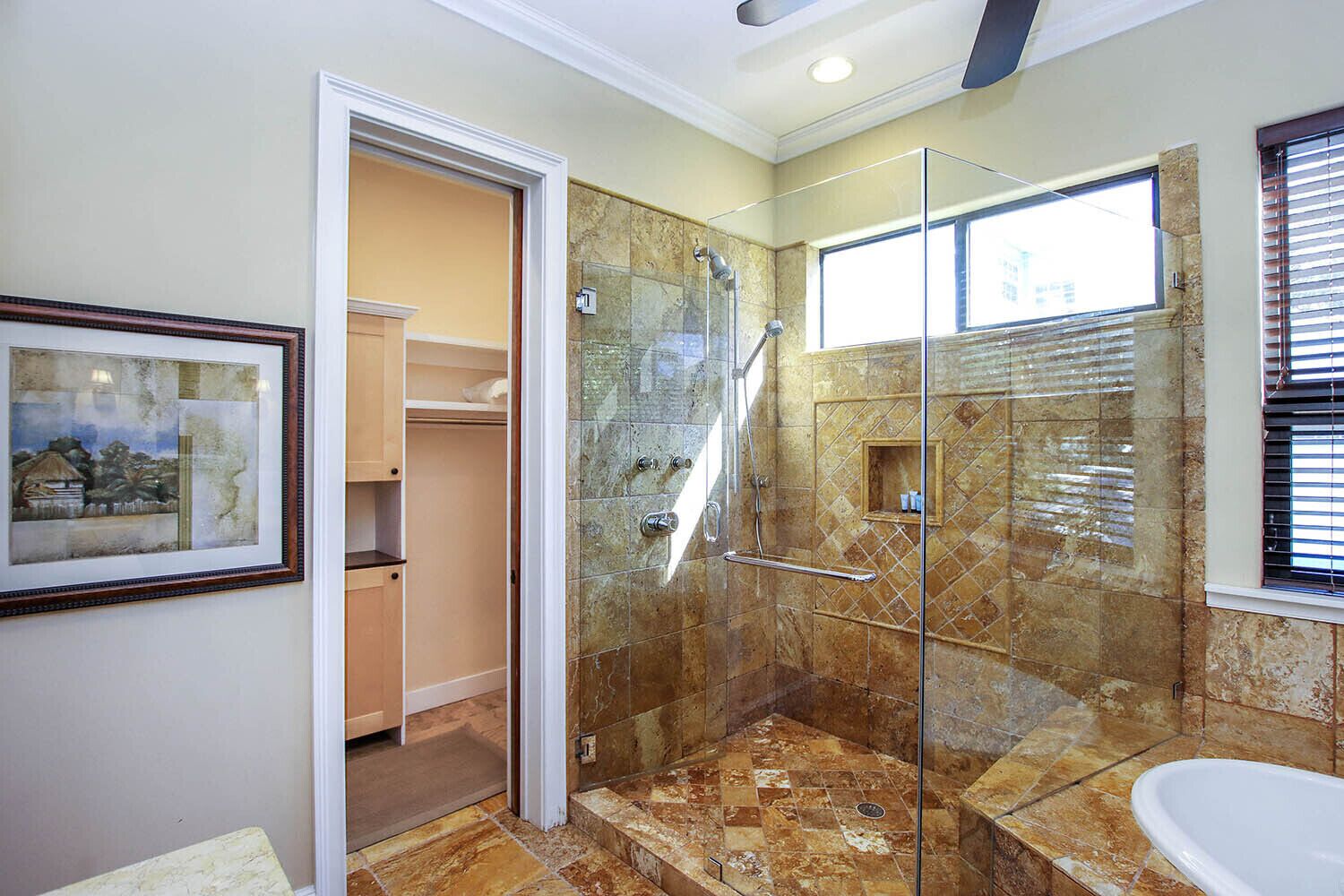 A modern bathroom with a glass-enclosed shower, a walk-in closet, and a large window.
