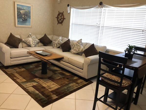 A living room with a sofa, coffee table, and a dining area with a chair and table. - Blocks to the Beaches (Naples)
