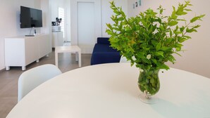 A modern living room with a white round table, a blue sofa, a flat-screen TV mounted on the wall, and a potted plant on the table.