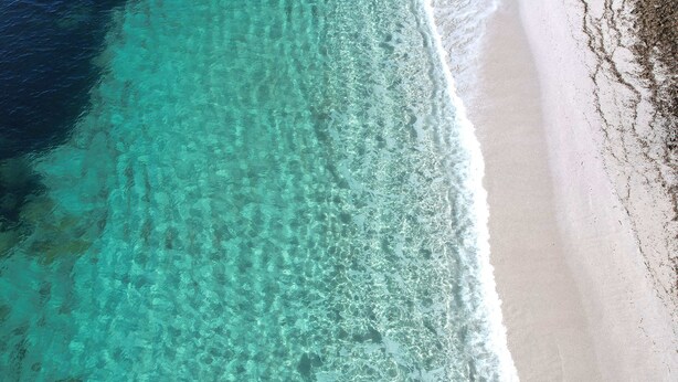 An aerial view of a beach with clear turquoise water and white sand.
