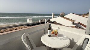 Eine Terrasse mit einem weißen Tisch und Stühlen, einer Weinflasche und Obst. Von der Terrasse hat man Blick auf den Ozean.