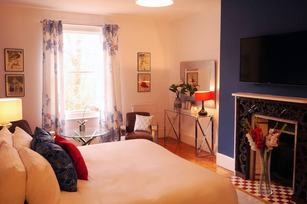 A hotel room with a large bed, a TV, a fireplace, and a window with curtains.