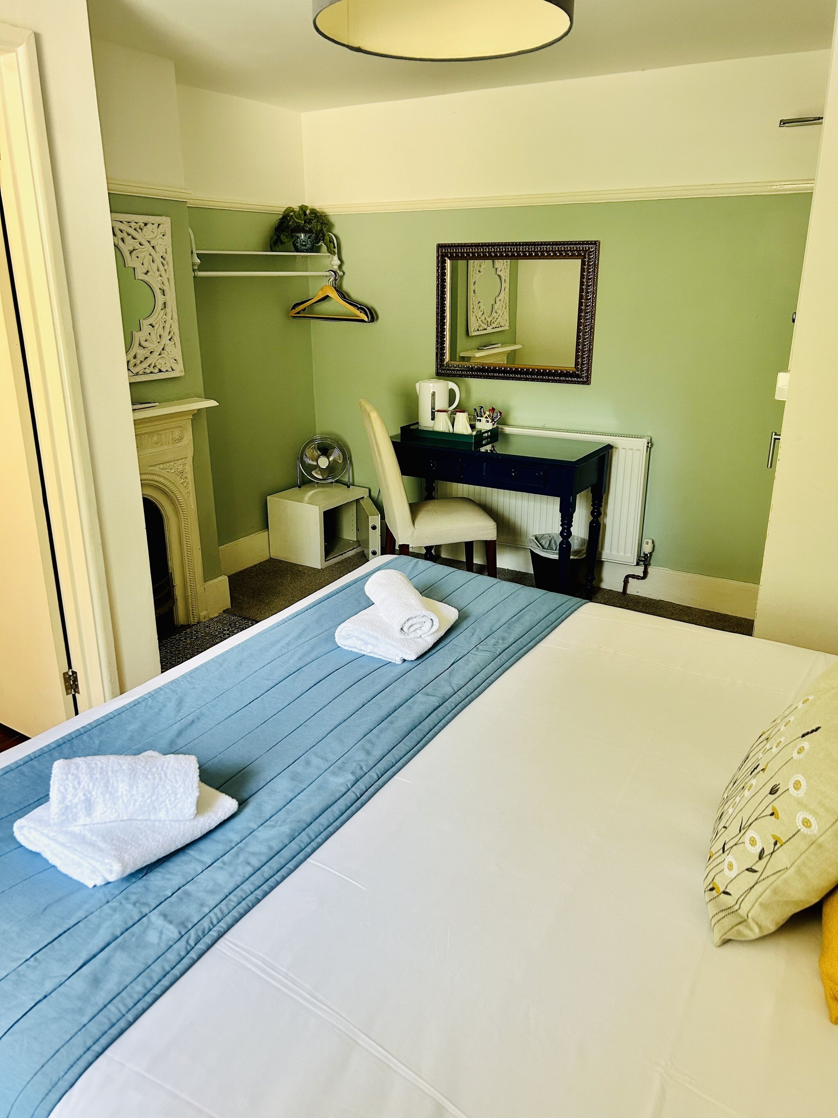 A hotel room with a bed, a desk, a chair, a mirror, and a radiator.