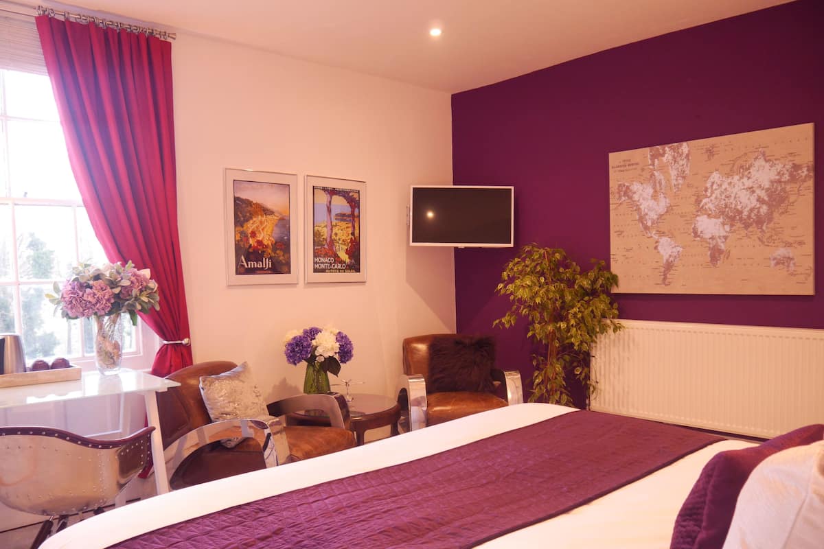 A hotel room with a bed, a desk with a chair, a TV, and a world map on the wall.