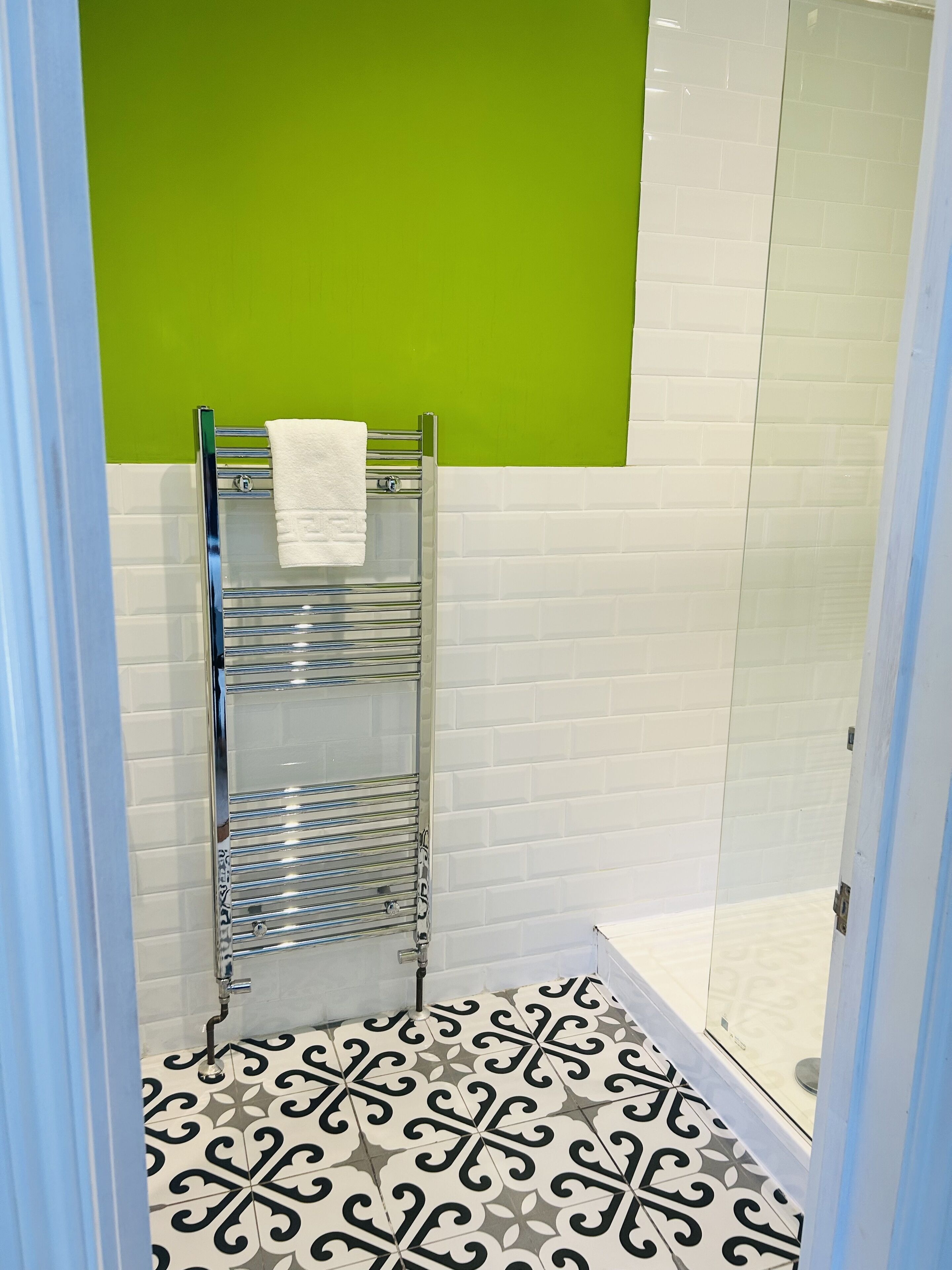 A bathroom with a shower, a towel rack, and patterned floor tiles.