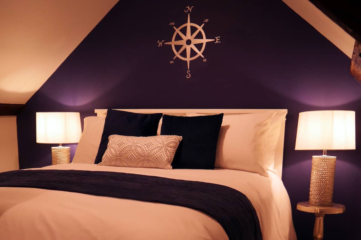 A bedroom with a bed, two bedside lamps, a compass wall decoration, and a dark blue accent pillow.