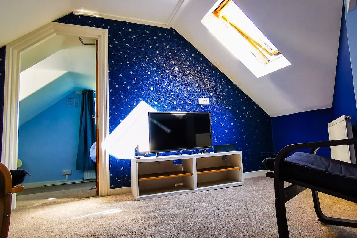 A room with a sloped ceiling, a TV on a white stand, a bunk bed, and a star-patterned wall.