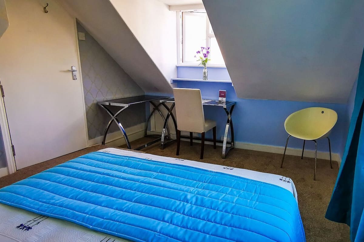 A bedroom with a bed, a desk, a chair, and a window.