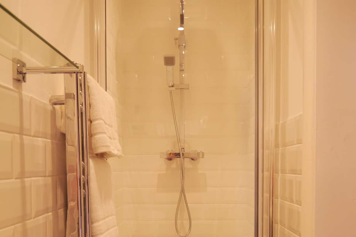 A glass-enclosed shower with a handheld showerhead, a glass door, and a white towel hanging on a rack.