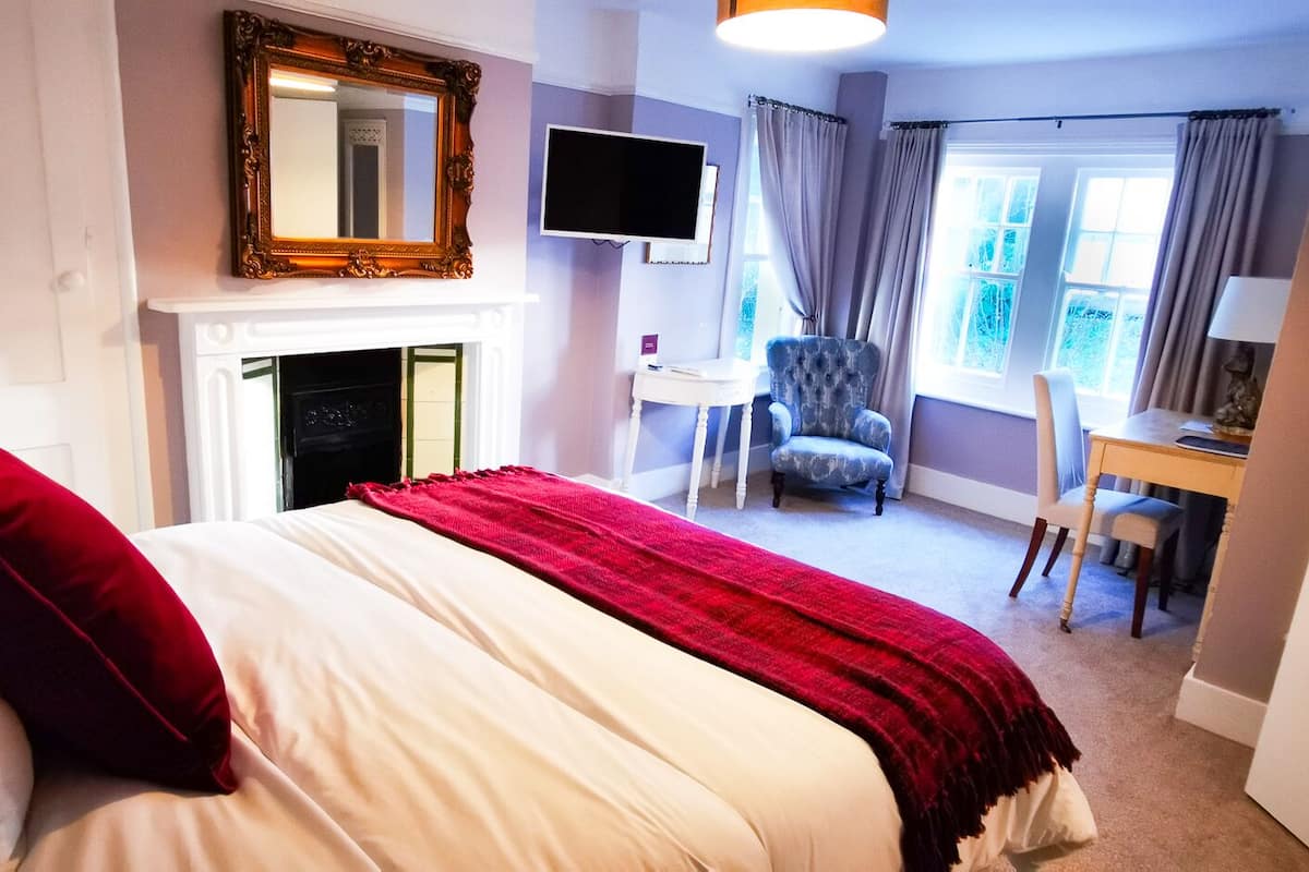 A bedroom with a bed, a television, a chair, a desk, and a fireplace.