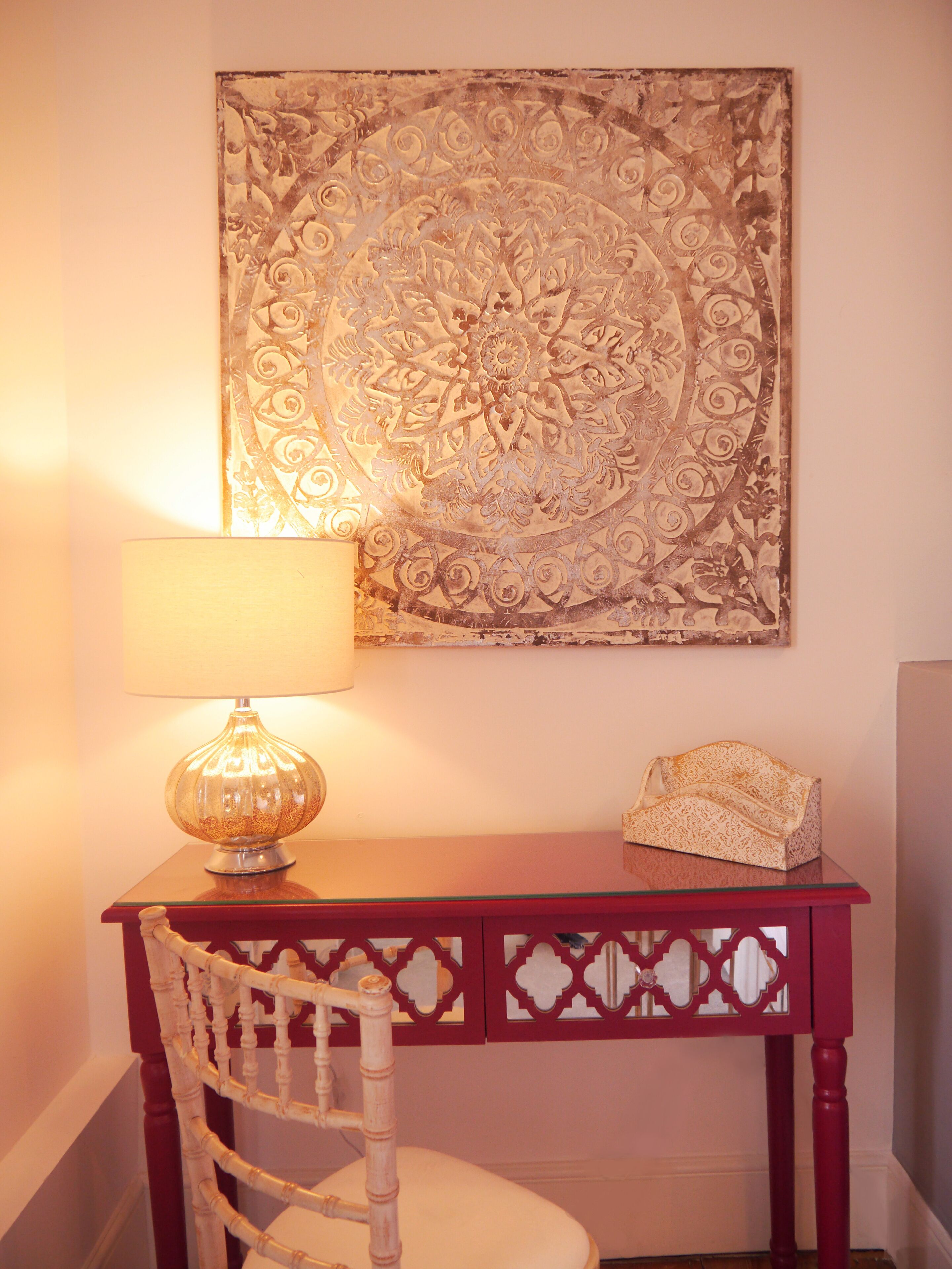 A wooden desk with a lamp and a decorative wall hanging.
