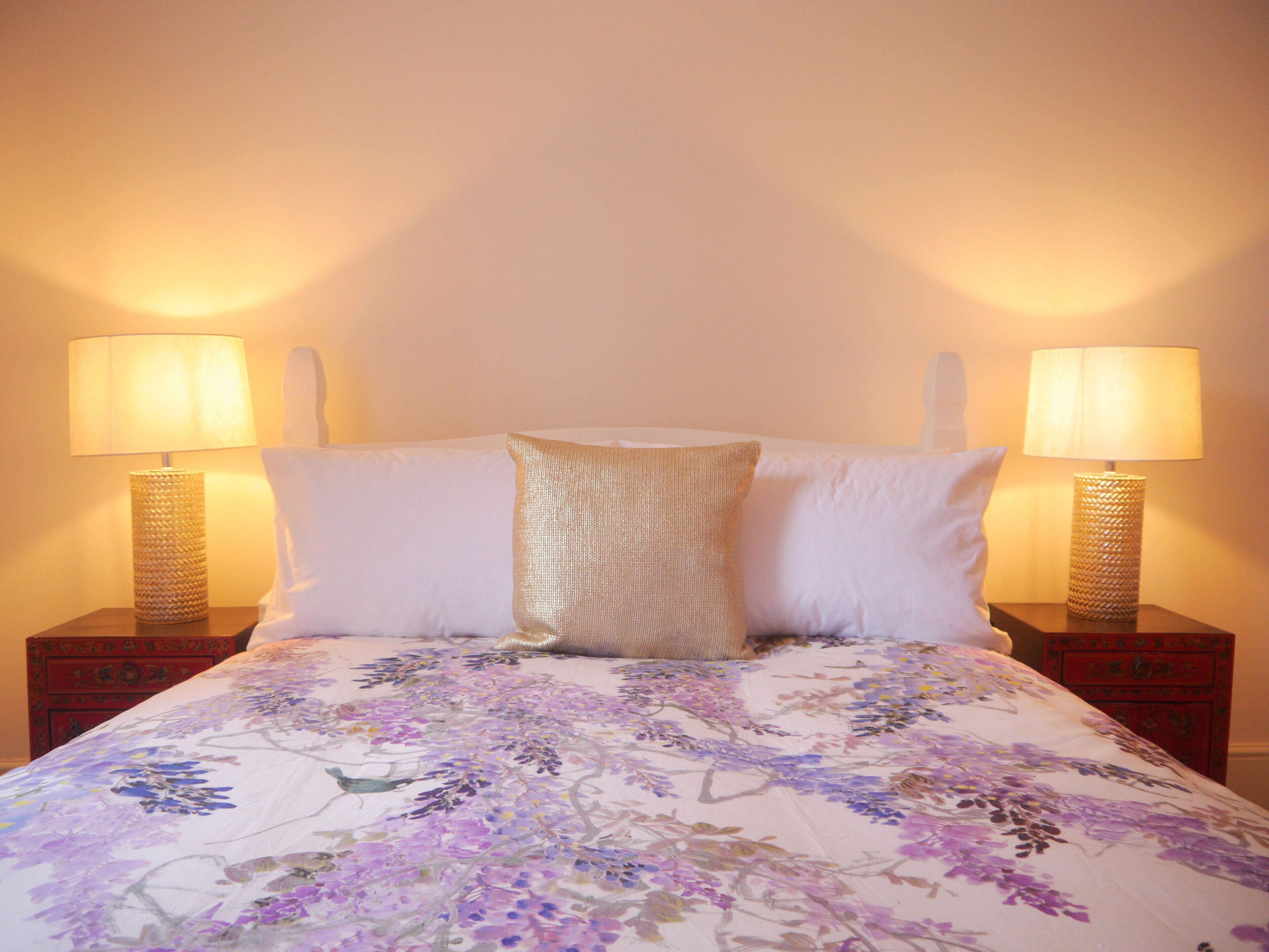 A bed with a floral bedspread, two bedside lamps, and a decorative pillow.