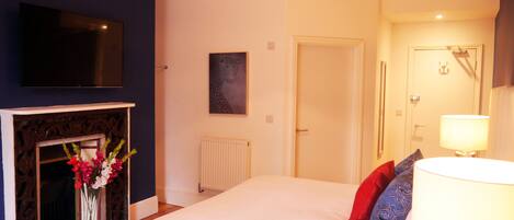 A bedroom with a large bed, a fireplace, a television on the wall, and a door leading to another room.